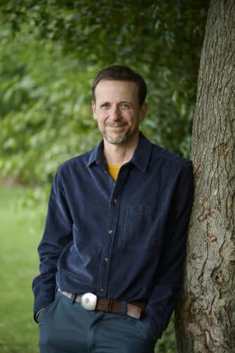 Portrait de Julien Perrot, appuyé contre le tronc d'un arbre